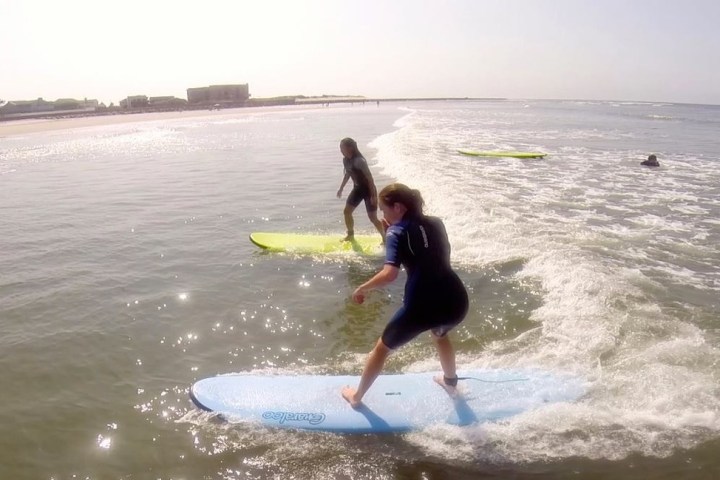 Three people surfing on small waves near a beach.