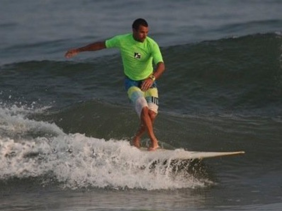 Person surfing on a wave in a green shirt and striped shorts.