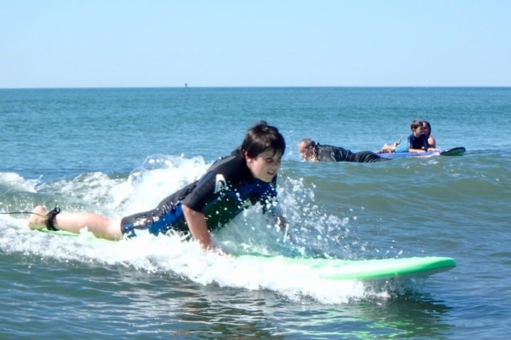 Boy surfing on small wave with people in the background.