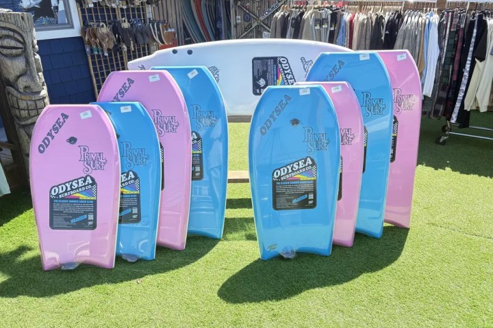 Blue and pink surfboards displayed on grass outside a shop.