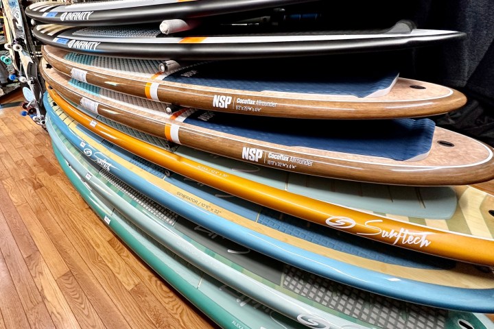 Stack of various surfboards on a wooden floor in a shop.
