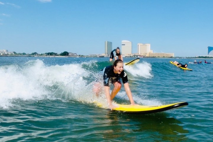 People surfing on yellow boards in the ocean with city skyline in the background.