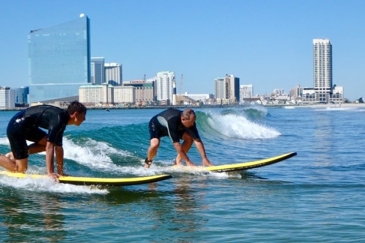 Two surfers on yellow boards riding waves near a city skyline.