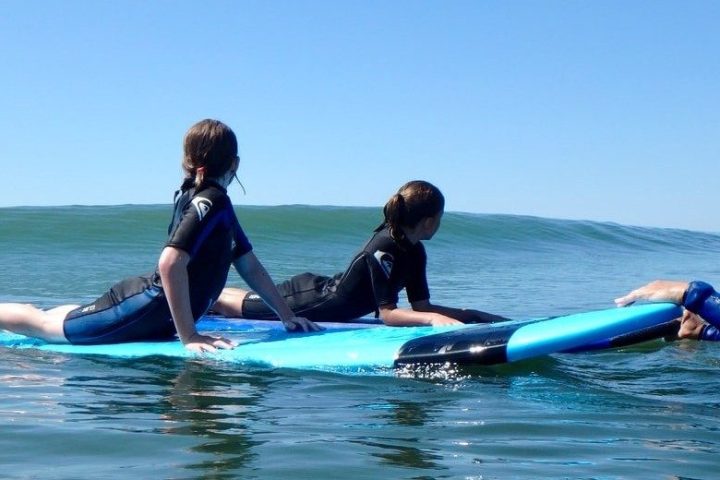 Two people on surfboards with instructor in calm ocean water.