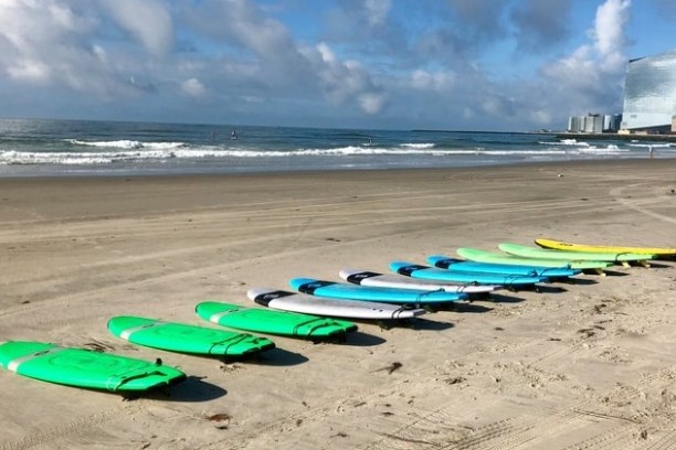 Surfboards lined up on a sandy beach with buildings in the background.