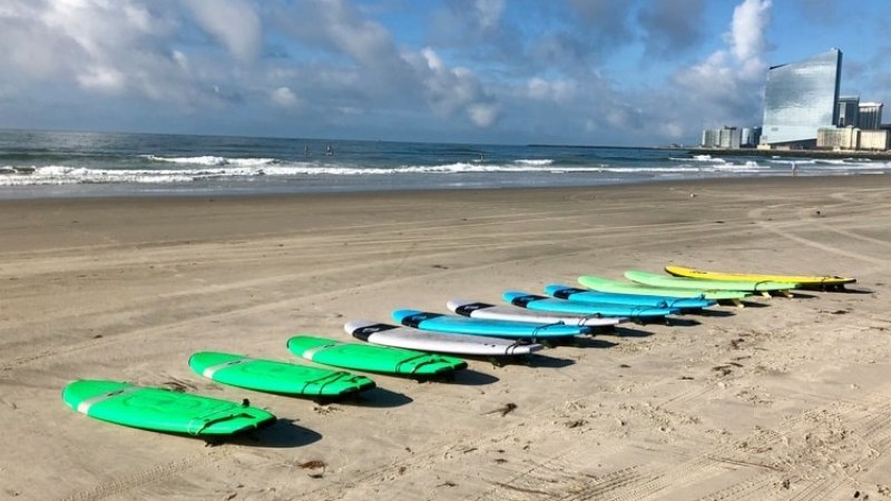 Surfboards lined up on a sandy beach with buildings in the background.