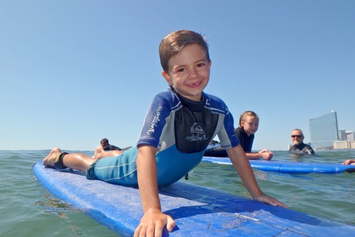 Smiling child in wetsuit on surfboard in the ocean.