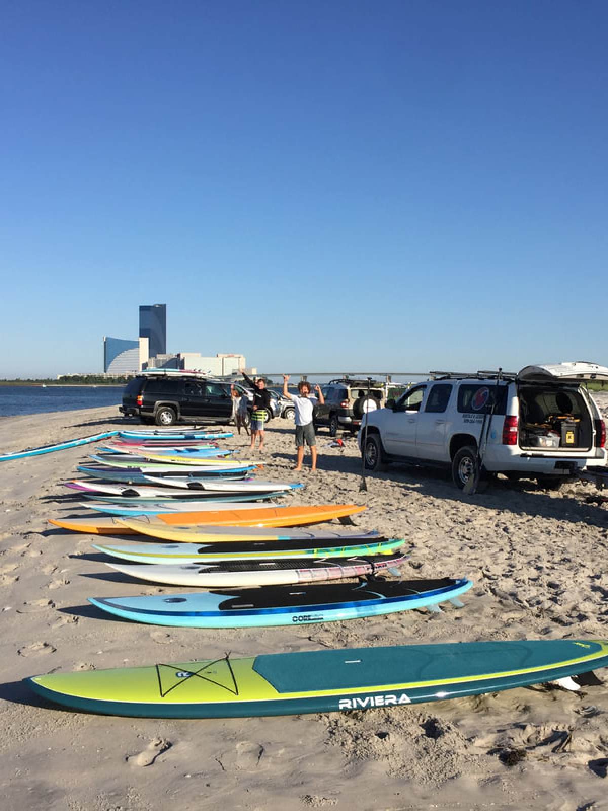 Colorful surfboards on a sandy beach with vehicles parked nearby.